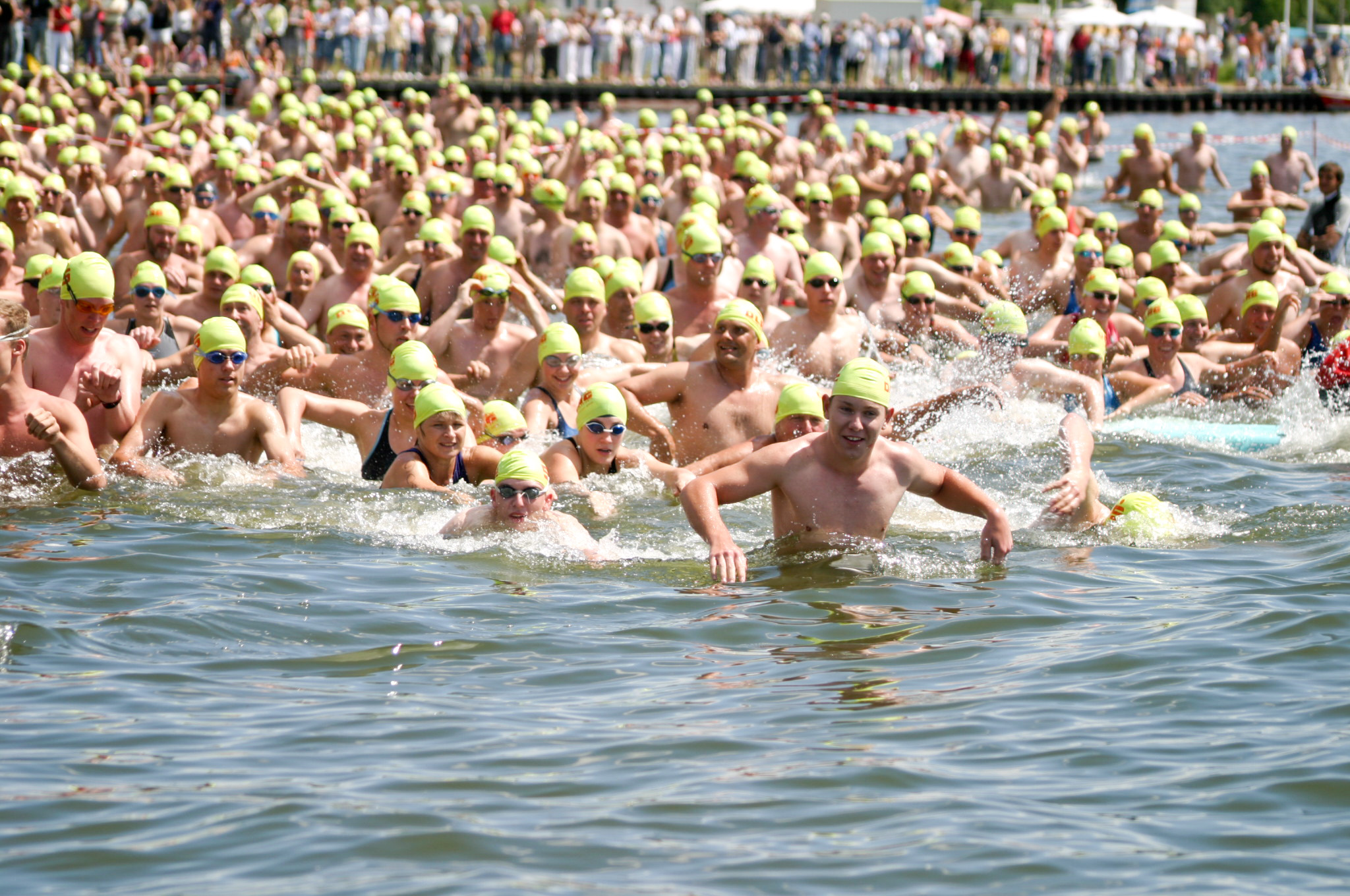 Viele Teilnehmende mit leuchtenden Badekappen starten gemeinsam zu einem Freiwasserschwimmen.