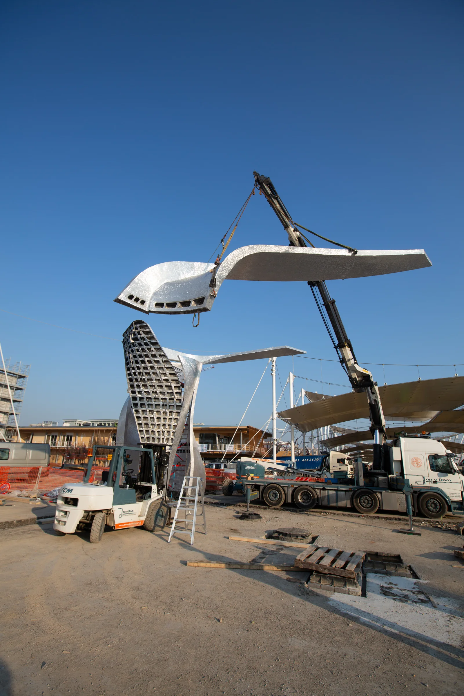 Große Metallskulpturen werden mit einem Kran auf einer Baustelle montiert.