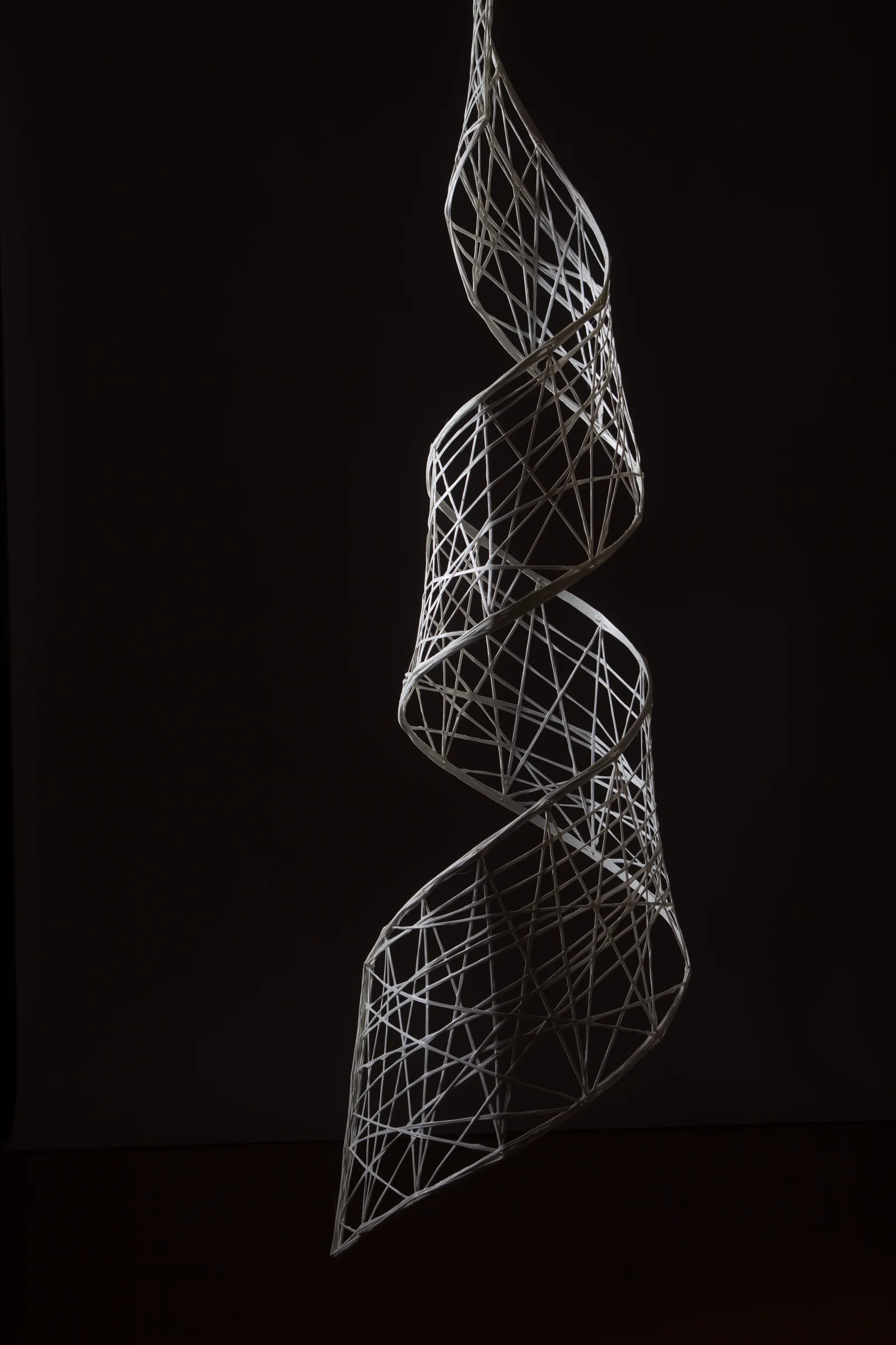 Detailaufnahme einer filigranen, spiralförmigen Metallskulptur vor dunklem Hintergrund.