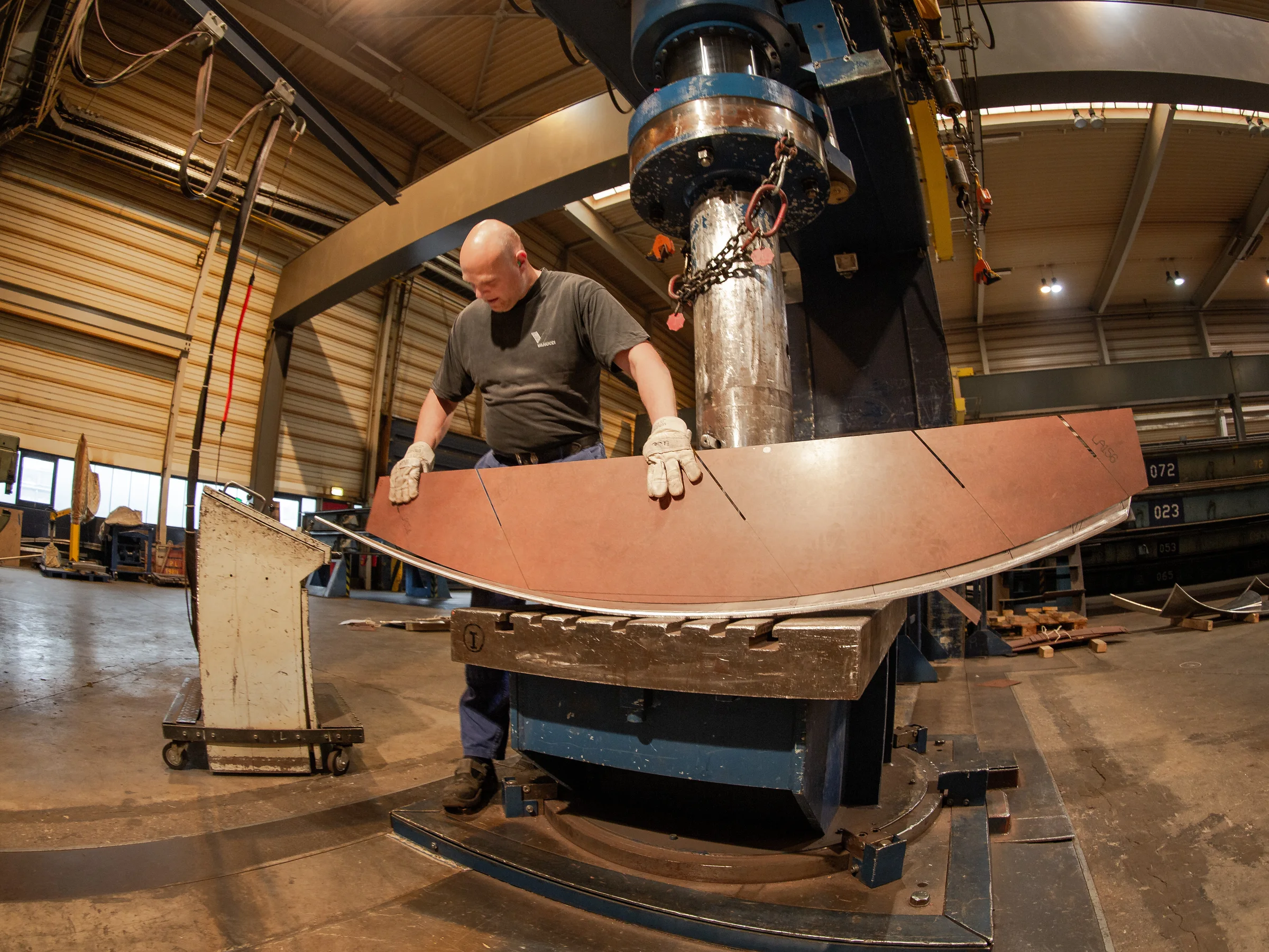 Ein Mitarbeiter kontrolliert ein gebogenes Metallbauteil an einer großen Umformmaschine.
